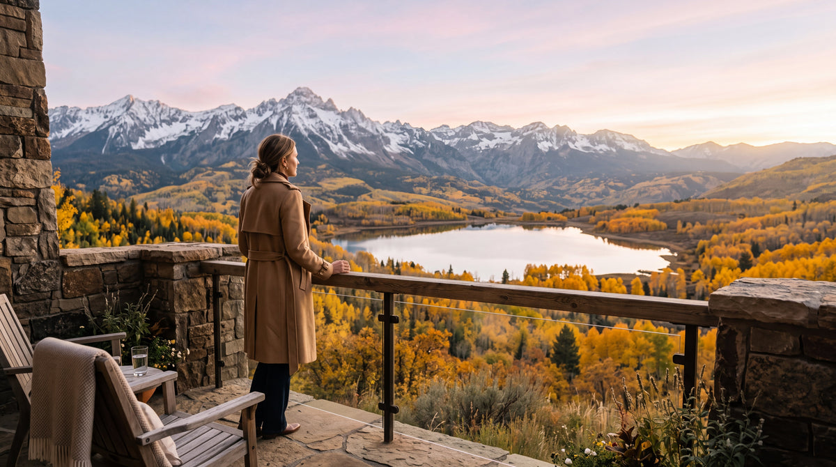 Spica Organics early-autumn editorial: a woman in a sand-colored trench coat overlooking a mountain lake framed by golden aspens at dawn.